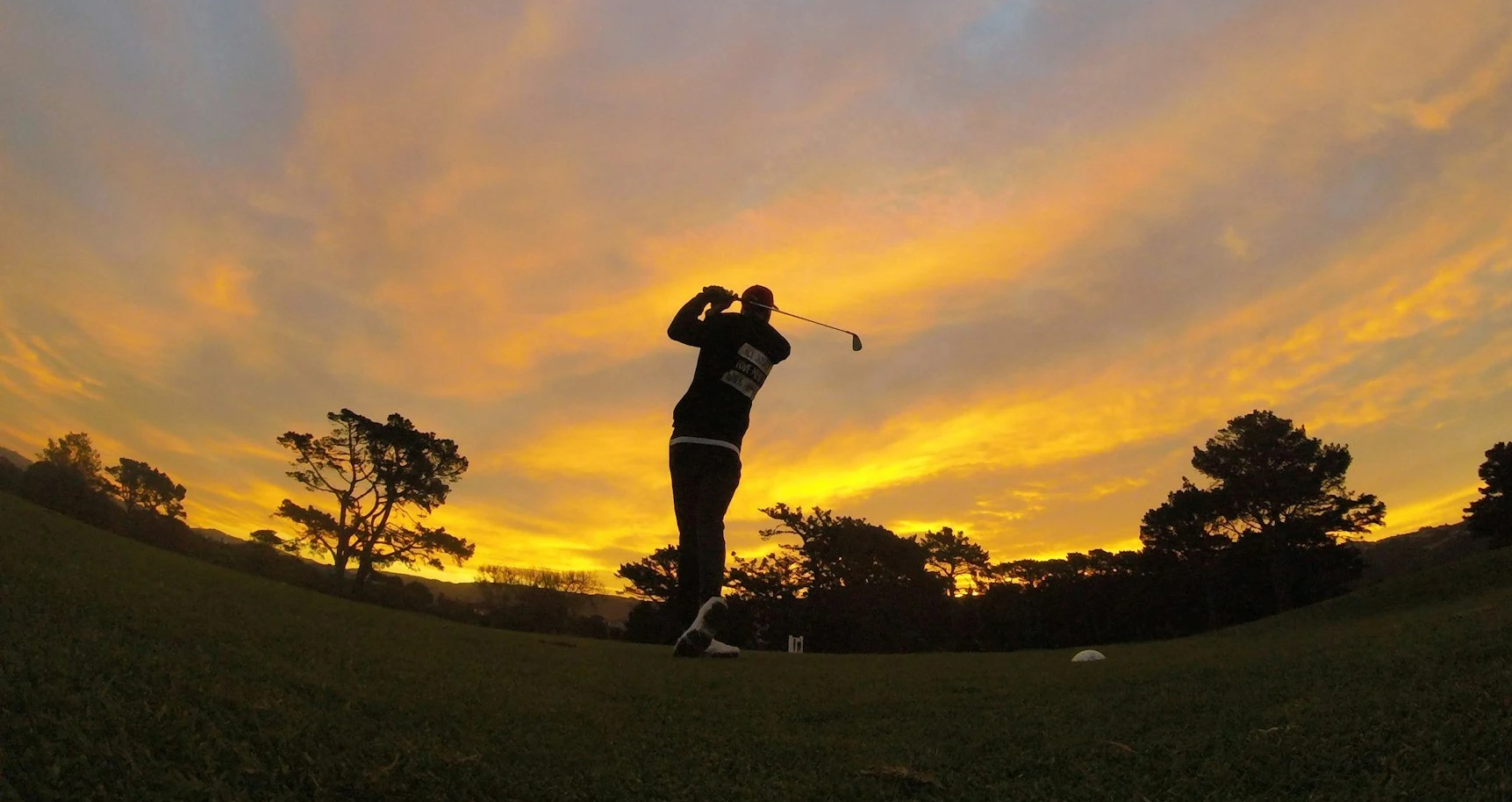 A golfer strikes a shot into the sunset